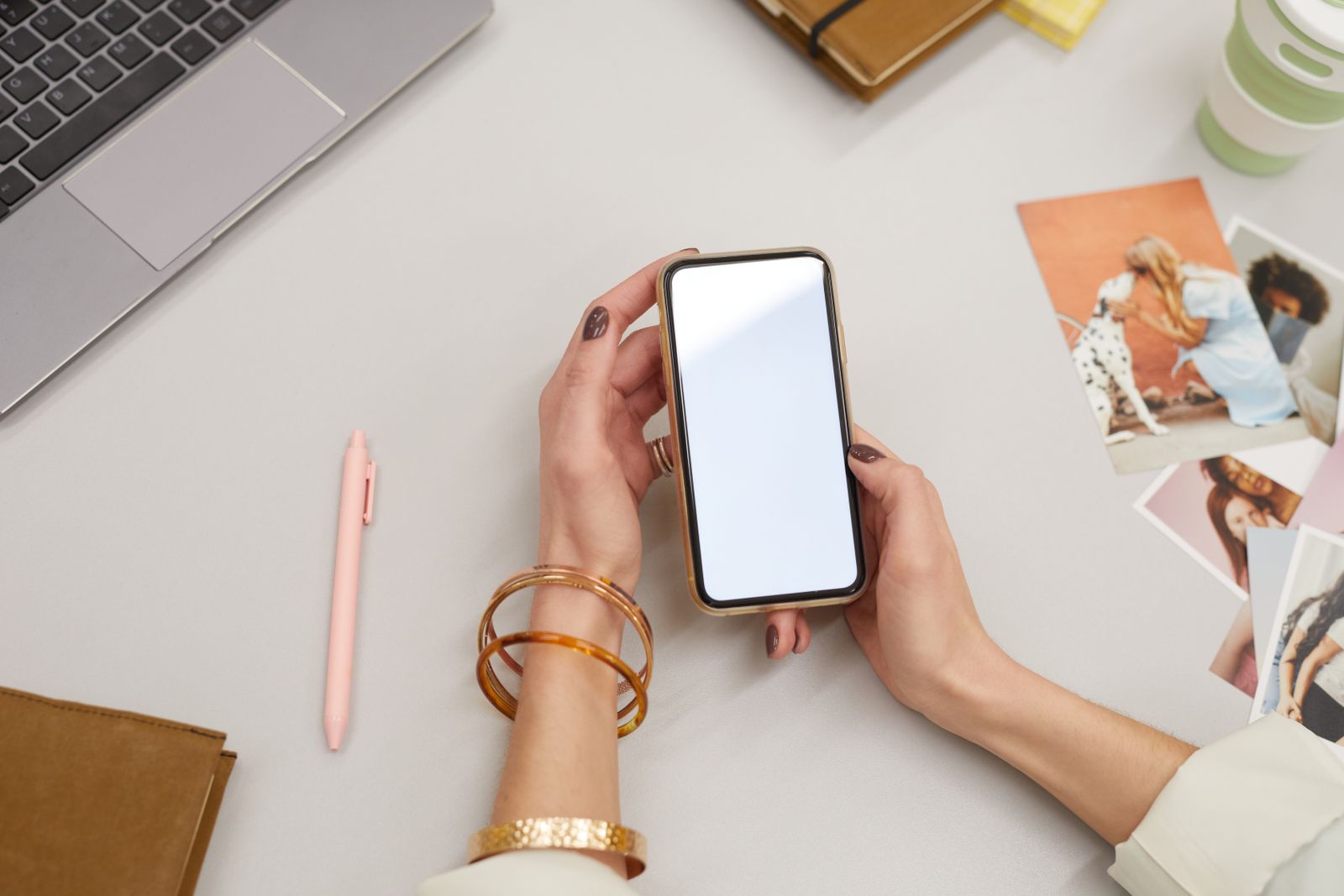Hands holding a phone at a desk beside a laptop and notebook — photo by Moe Magners on Pexels