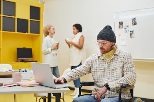 Man in wheelchair using a laptop in a casual office environment.