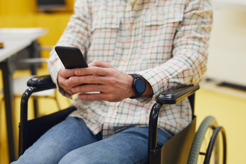 Adult using smartphone while seated in a wheelchair, wearing plaid shirt indoors.