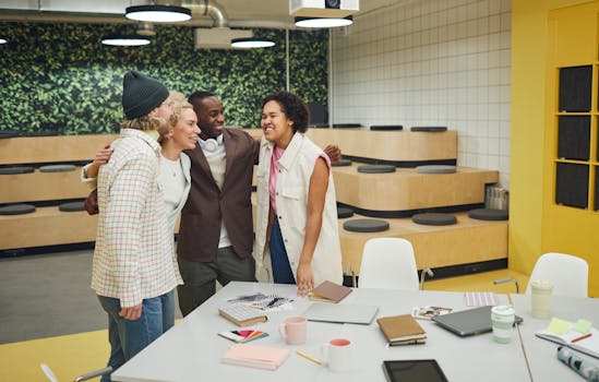 A diverse group of colleagues huddling and smiling in a modern office setting, promoting teamwork.