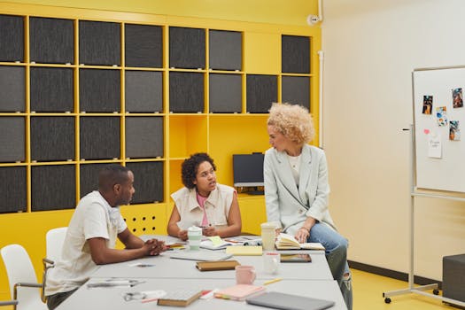 A diverse group of adults engaged in a teamwork discussion in a bright, modern office setting.