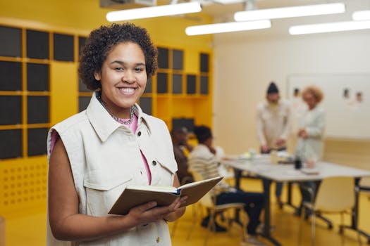 Smiling young woman holding a notebook in a vibrant classroom environment with group discussion.