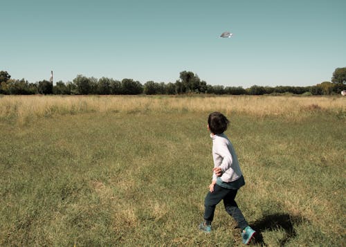 Boy Playing Paper Airplane on Grass Field