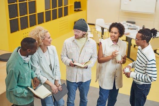Five diverse coworkers engaged in a casual team meeting in a bright, modern workspace.