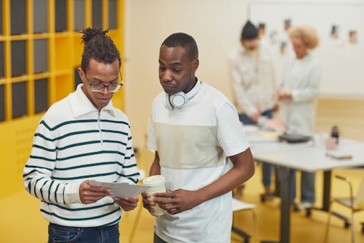 Two colleagues discussing work in a contemporary office environment with attentive coworkers in the background.