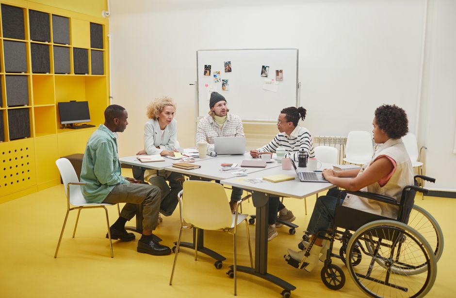 Un grupo diverso de compañeros de trabajo teniendo una reunión colaborativa alrededor de una mesa en una oficina moderna.