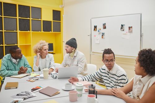 Free A diverse group of coworkers engaged in a creative meeting around a table in a bright, modern office space. Stock Photo