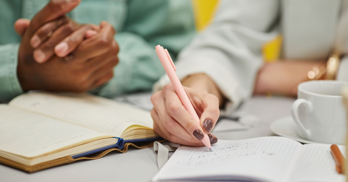 Close-up of diverse hands writing in notebooks with a pen during a meeting.