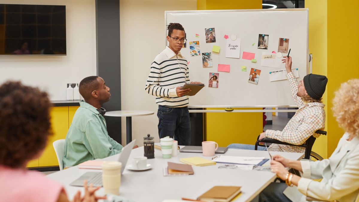A man explains a plan at a whiteboard while a team works through presentation problems together
