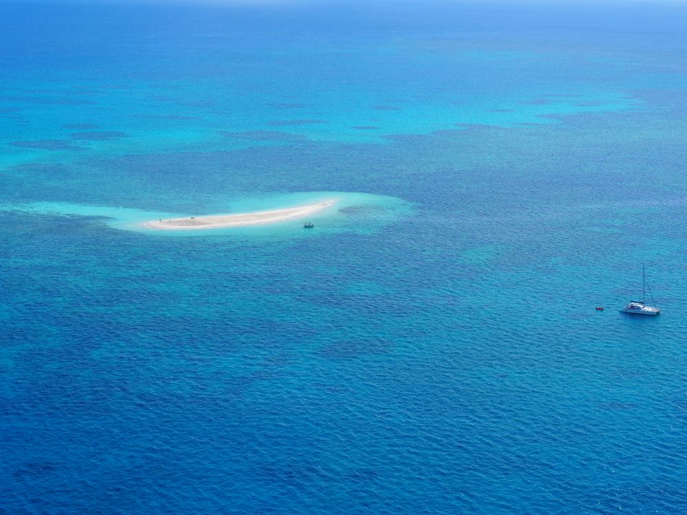 Cayo de arena solitario en mar turquesa de la Gran Barrera con velero al fondo