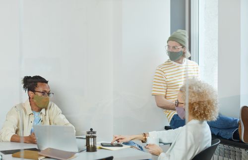 Free Colleagues engage in a team discussion while wearing face masks, highlighting pandemic office practices. Stock Photo