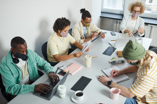 A diverse team collaborates in an office setting, wearing masks for safety.