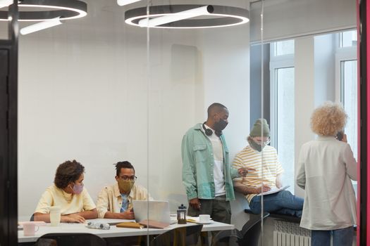 A group of diverse coworkers discussing in a modern office space while wearing face masks.