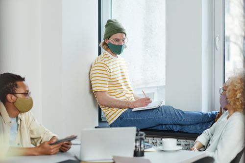 Free Three coworkers in masks have a brainstorming session in a modern office setting, reflecting pandemic work norms. Stock Photo