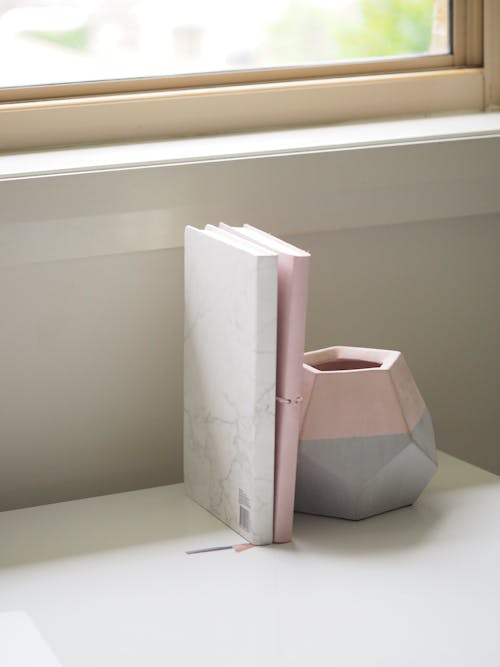 Livros Brancos E Rosa Empilhados Ao Lado De Um Vaso De Cerâmica Rosa E Cinza