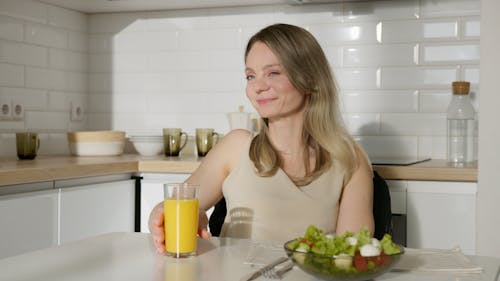 Woman Sitting By The Table With An Orange Juice and Vegetable Salad