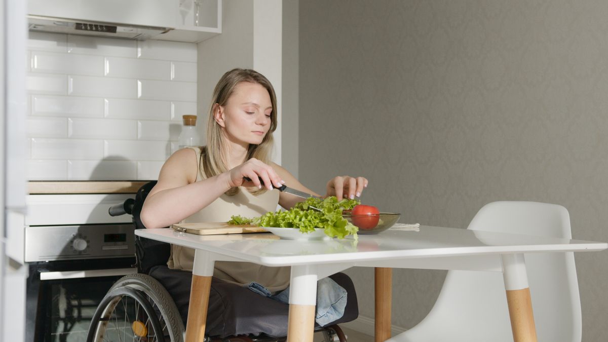 A woman using a wheelchair preparing vegetables at a kitchen table