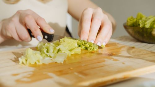 Free A person slices fresh lettuce on a wooden cutting board, showcasing food preparation techniques. Stock Photo