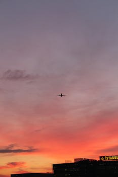 A silhouette of an airplane flying over Istanbul during a vibrant sunset with dramatic clouds.