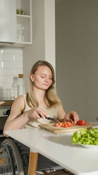 A woman in a wheelchair is slicing tomatoes on a cutting board in a modern kitchen.
