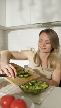 Smiling woman cutting cucumbers in a bright kitchen, a modern take on healthy lifestyle.