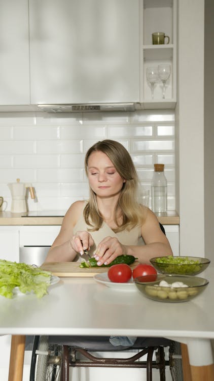 Free A Woman Sitting at the Table Slicing a Zucchini Stock Photo