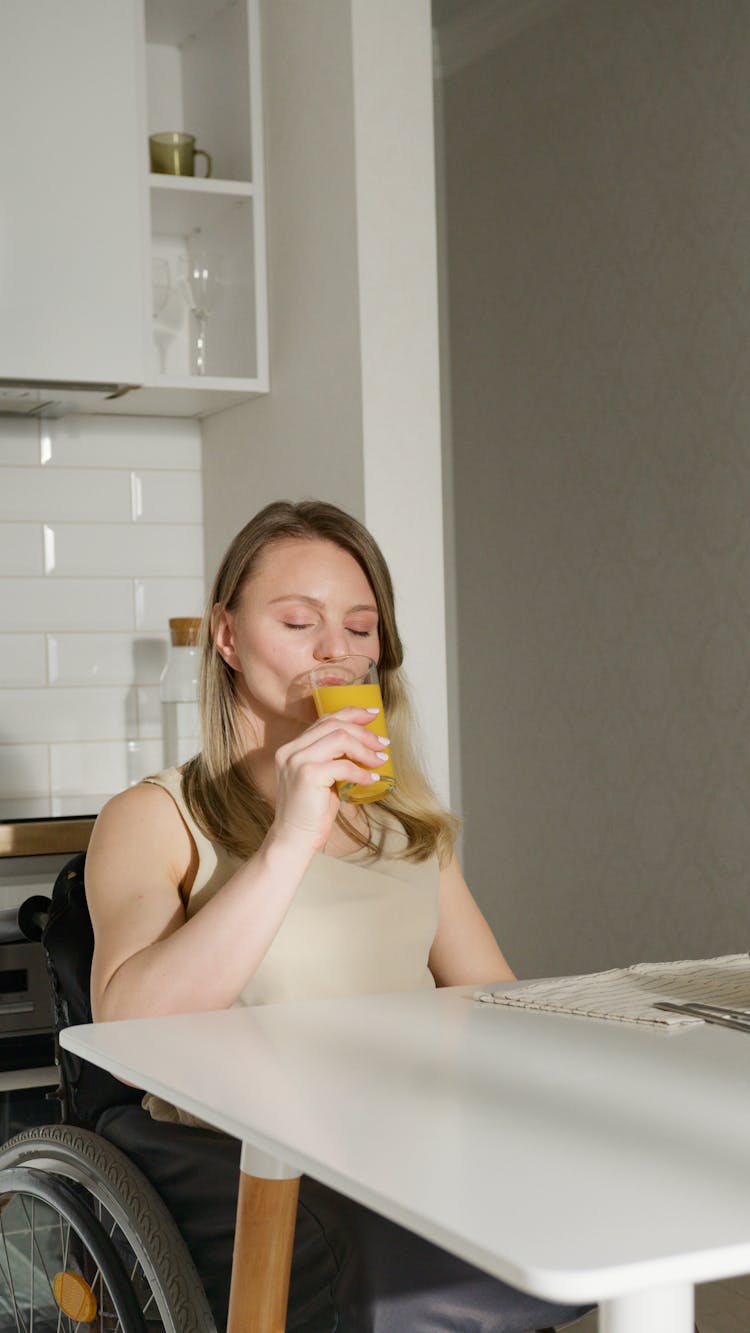 A Woman Sitting On A Wheelchair Drinking A Glass Of Juice