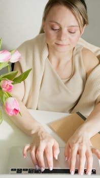 Businesswoman working on a laptop with tulips on desk, creating a serene workspace vibe.