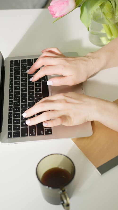 Free Hands typing on a laptop, with a pink tulip and coffee nearby on a desk Stock Photo