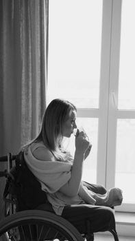 Black and white photo of a woman in a wheelchair gazing out a window with a contemplative expression.
