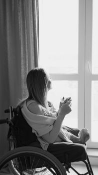 Black and white image of a woman in a wheelchair gazing through a window.
