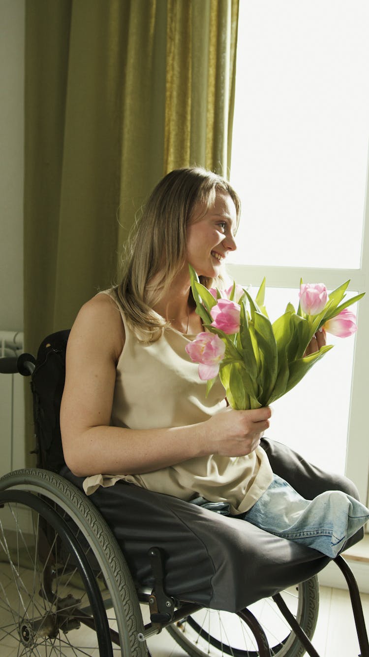 A Woman In Beige Tank Top Holding Pink Flowers With Green Leaves