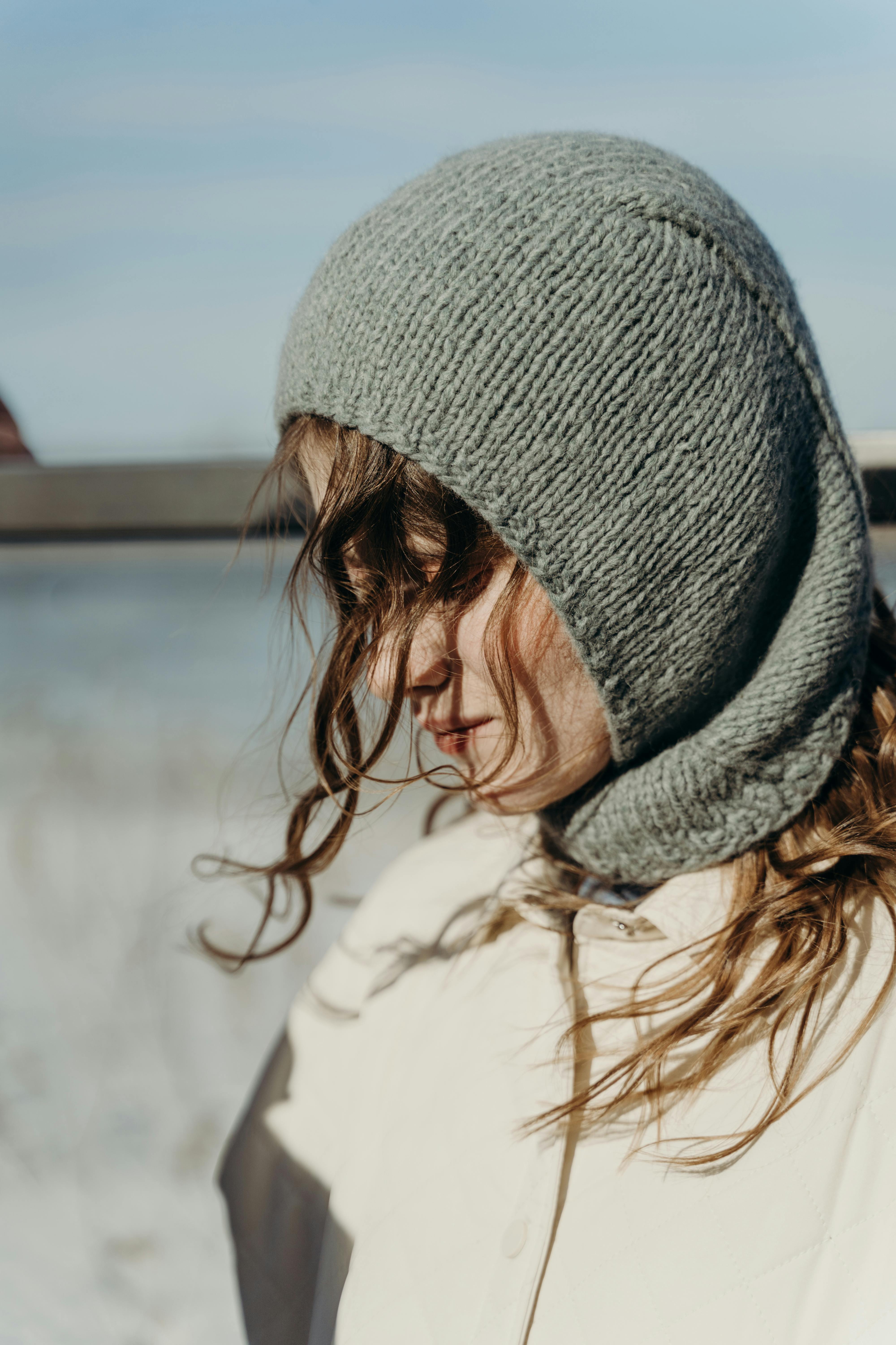 A woman wearing a green knit balaclava, captured in soft natural light outdoors.