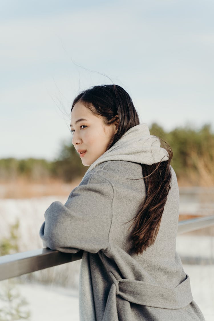 A Woman In Gray Winter Clothing Leaning On A Railing