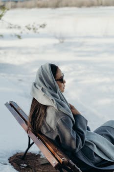 Asian woman in winter clothing sitting on a bench in a snowy outdoor setting.