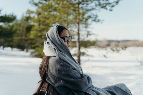 Free Woman in a grey coat with sunglasses enjoying the snow outdoors during winter. Stock Photo