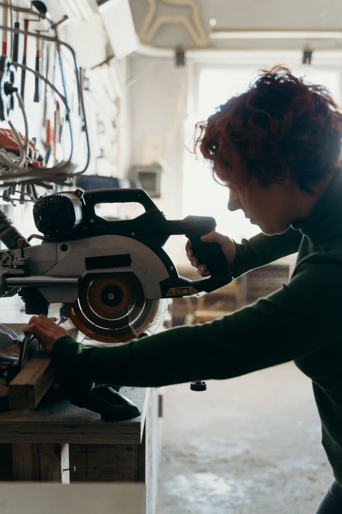 Free A woman focuses intensely while using a miter saw in a workshop setting. Stock Photo
