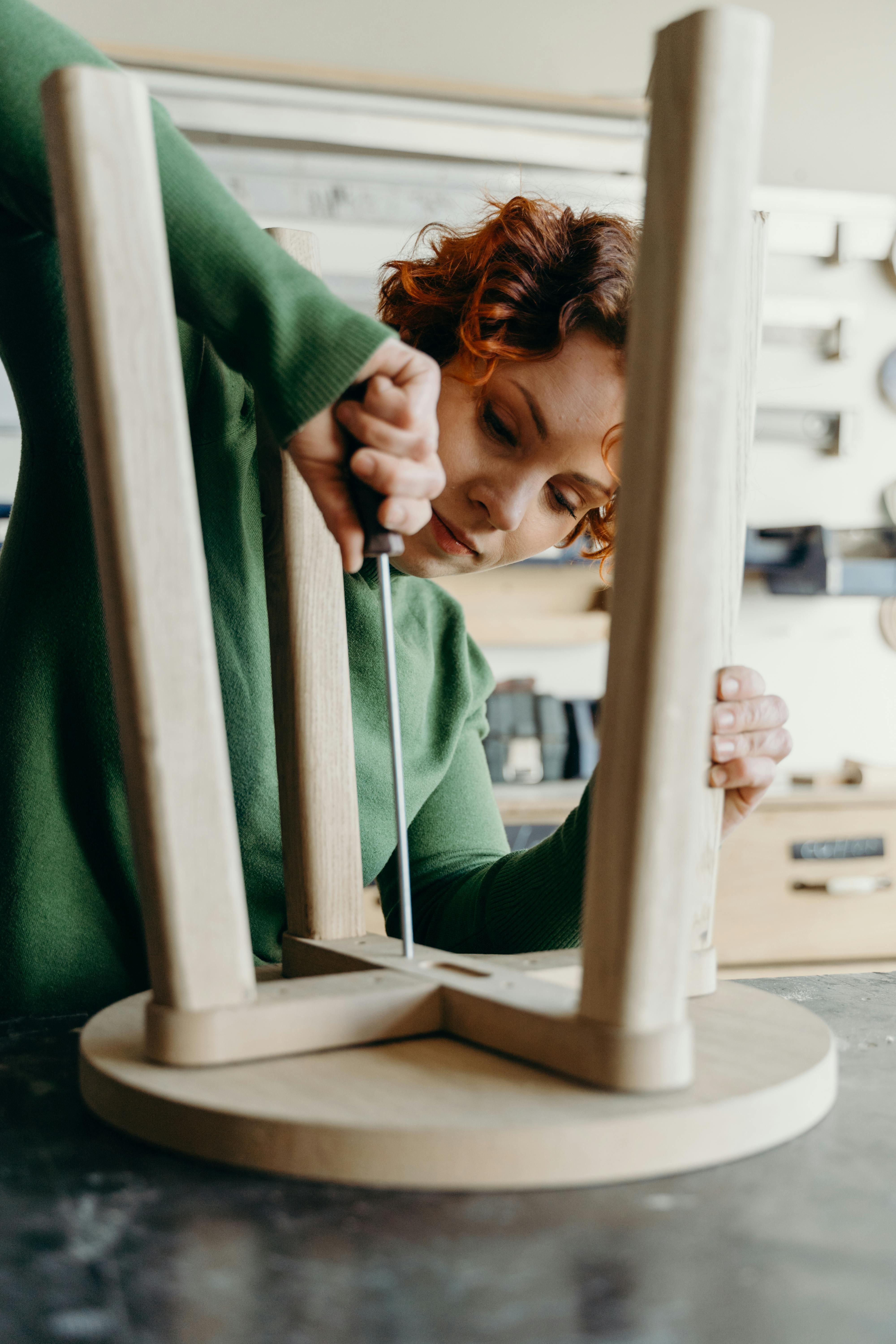 Woman in workshop assembling a wooden chair using hand tools.