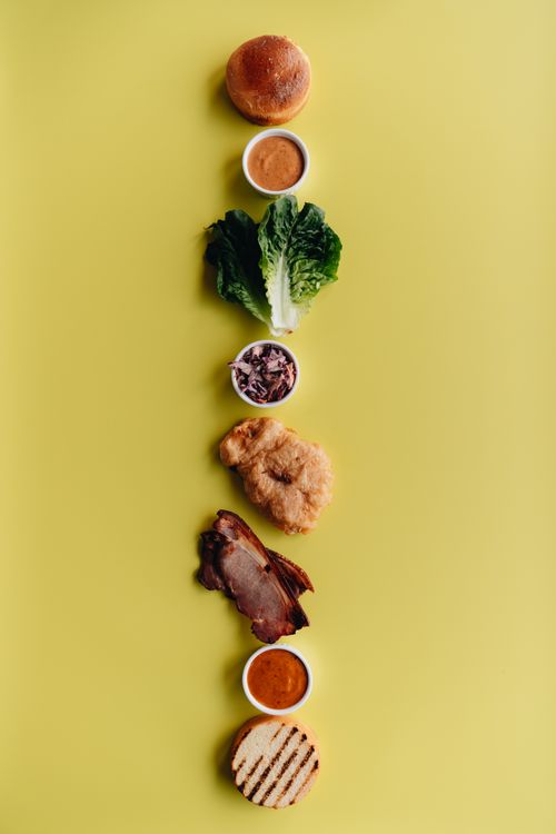 Free A visually appealing deconstructed burger with fresh ingredients arranged on a vibrant yellow background. Stock Photo