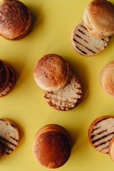 Top view of multiple burger buns with grill marks on a vibrant yellow background.