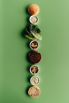 Artistic presentation of a deconstructed burger with various ingredients on a green backdrop.
