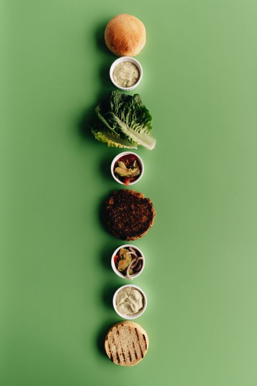 Free Artistic presentation of a deconstructed burger with various ingredients on a green backdrop. Stock Photo