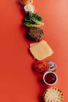 A deconstructed burger with ingredients lined up on a vibrant red background.