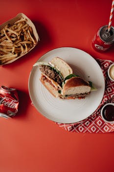 Top view of a burger meal with fries and soda on a vibrant red background.