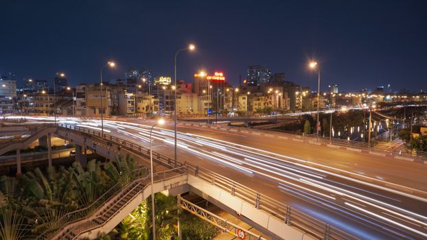 Dynamic cityscape at night showcasing light trails on a busy road under bright streetlights.