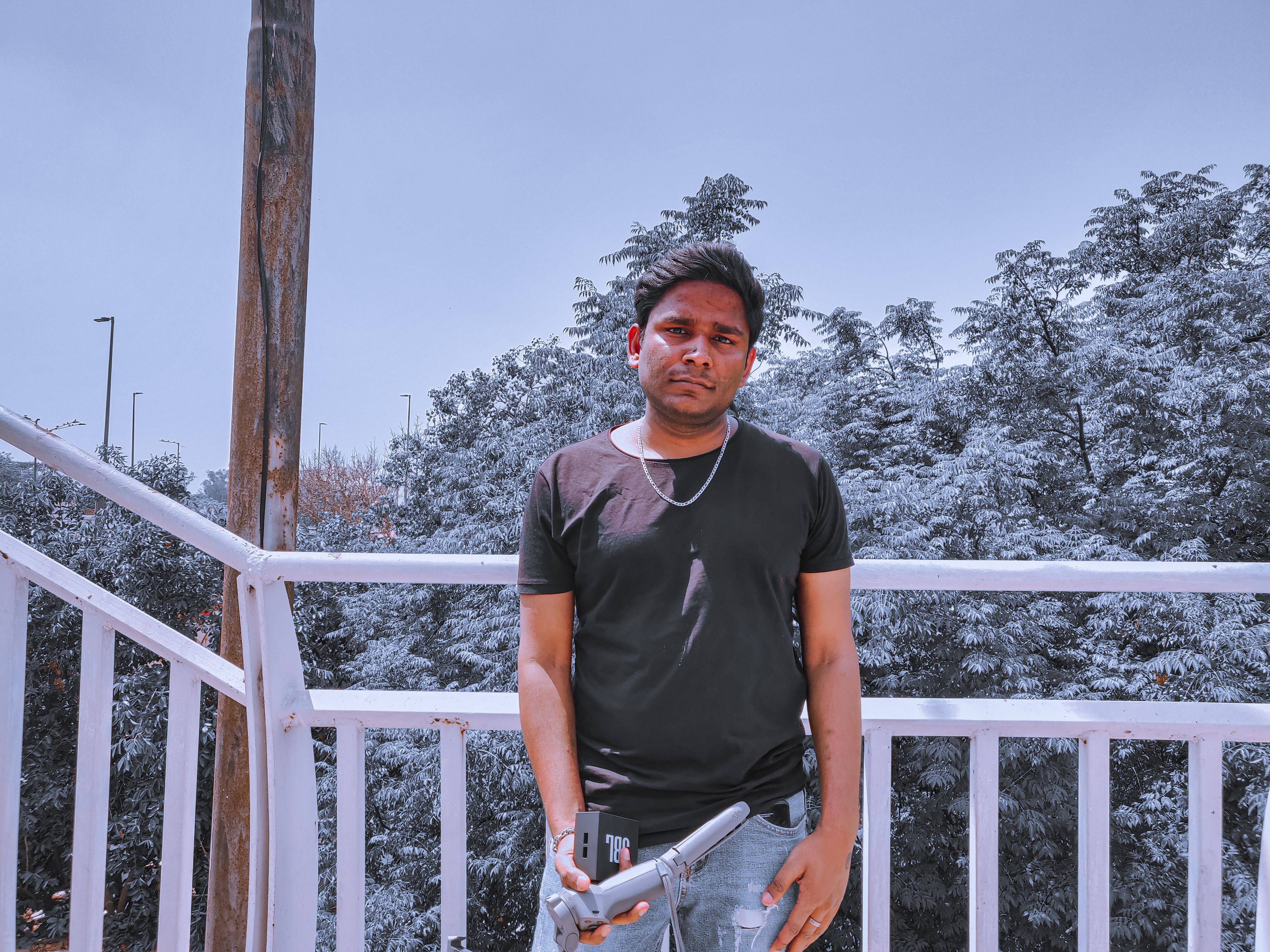 Man in black shirt holding a gadget outdoors with a scenic background of trees.