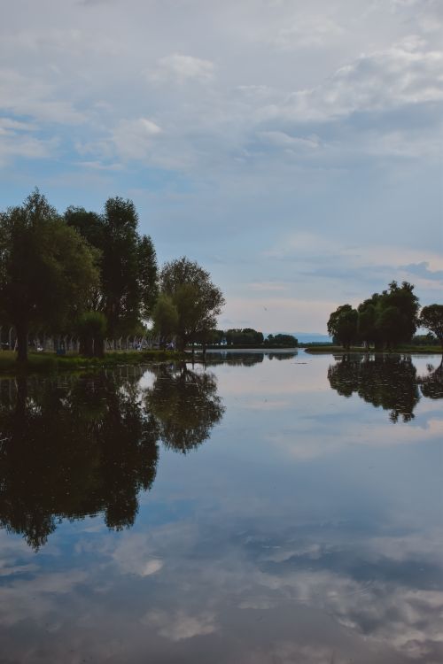Free Peaceful lake landscape with tree reflections and a vast blue sky. Stock Photo