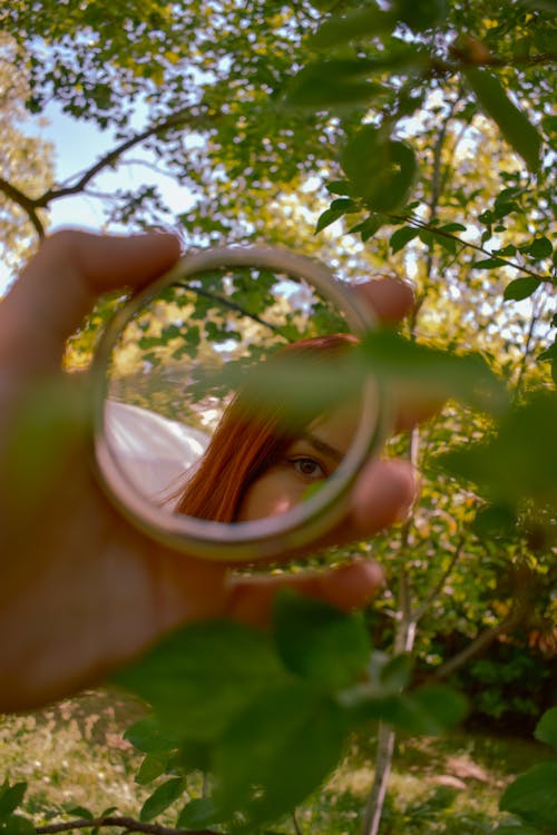 Person's Hand Holding a Mirror with a Reflection of a Woman with Red Hair