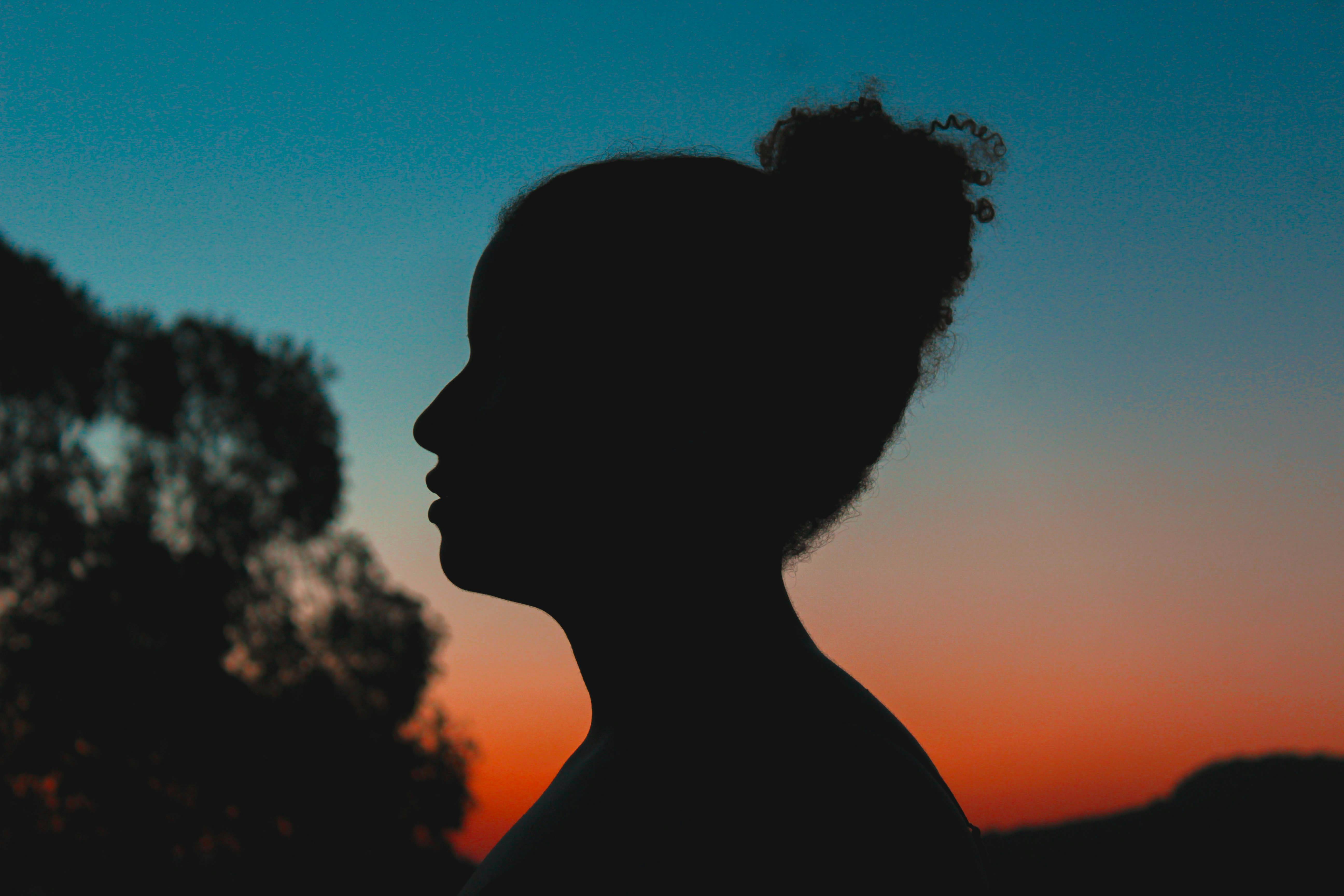 Silhouette of a person against a vibrant sunset background with trees.