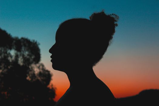 Silhouette of a person against a vibrant sunset background with trees.